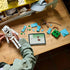 LEGO Minecraft The Skeleton build in white and gray bricks is held over a wooden table beside turquoise pieces, a brown bow and a tablet displaying digital building instructions.