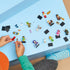 LEGO Minifigures Series 29 toys spread across a light blue tabletop with colorful plastic character figures, black display bases, and a child assembling pieces during play.