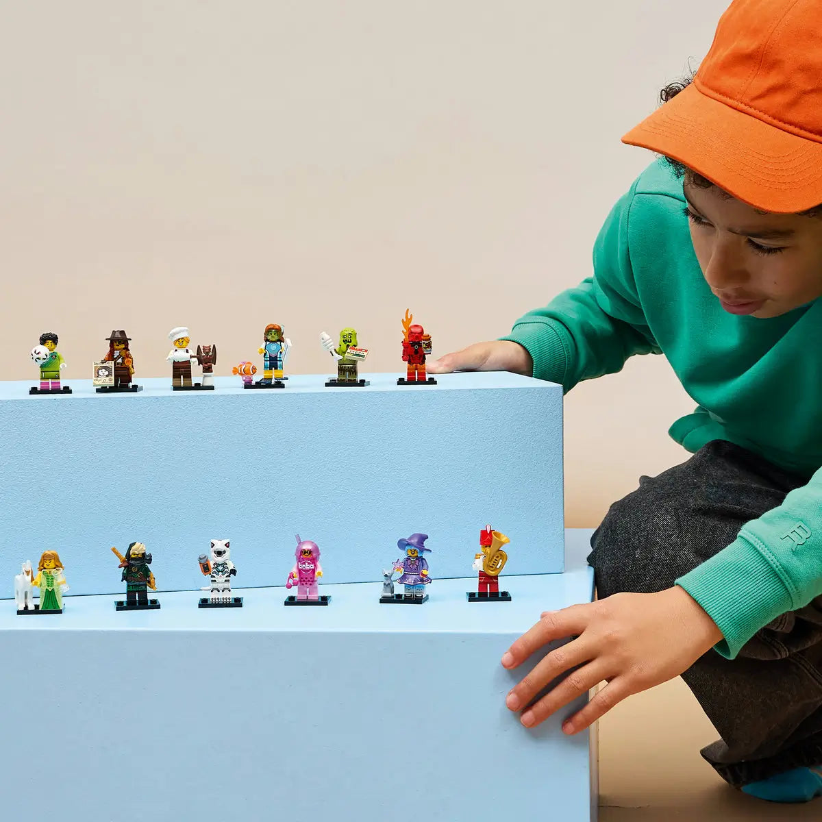 LEGO Minifigures Series 29 collectible figures stand on light blue display blocks as a child in an orange cap arranges colorful plastic characters in a neutral indoor setting.