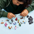 LEGO Shrek minifigures and accessories are spread across a light blue tabletop while a child assembles pieces, with black display bases grouped at the right.