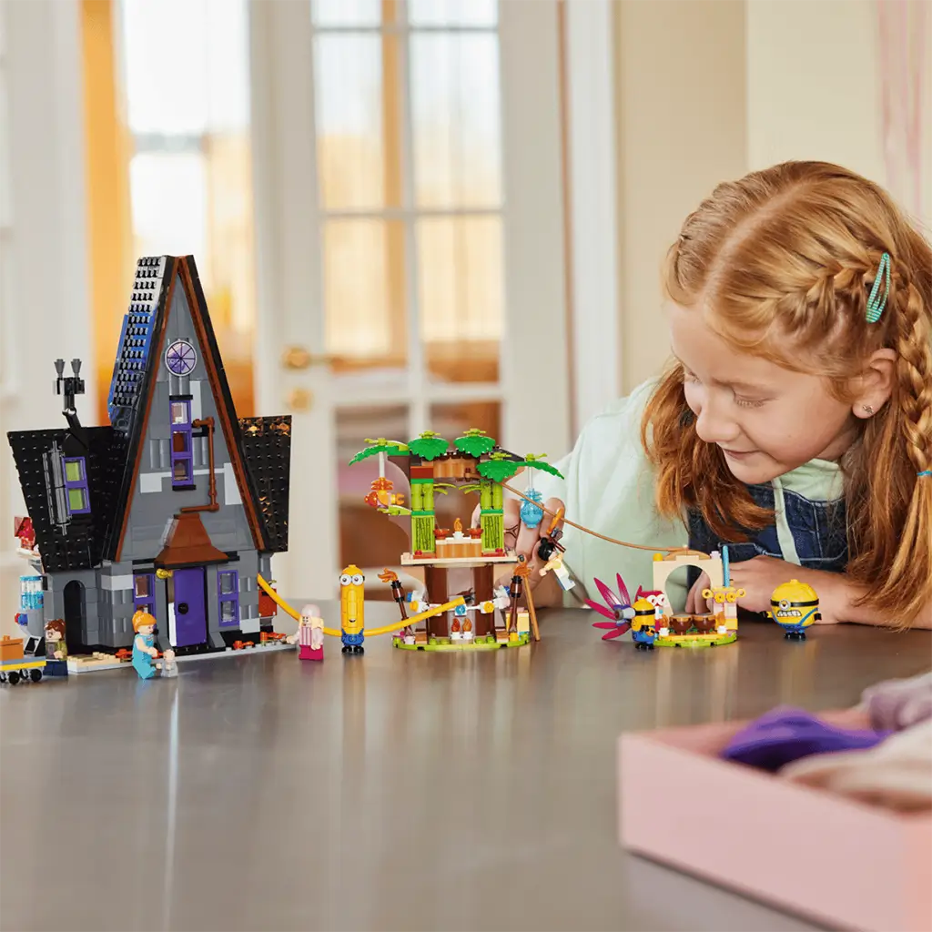LEGO Despicable Me 4 playset in gray, green and yellow plastic bricks sits on a table as a child plays with Gru’s mansion, treehouse, zip line and Minion figures.