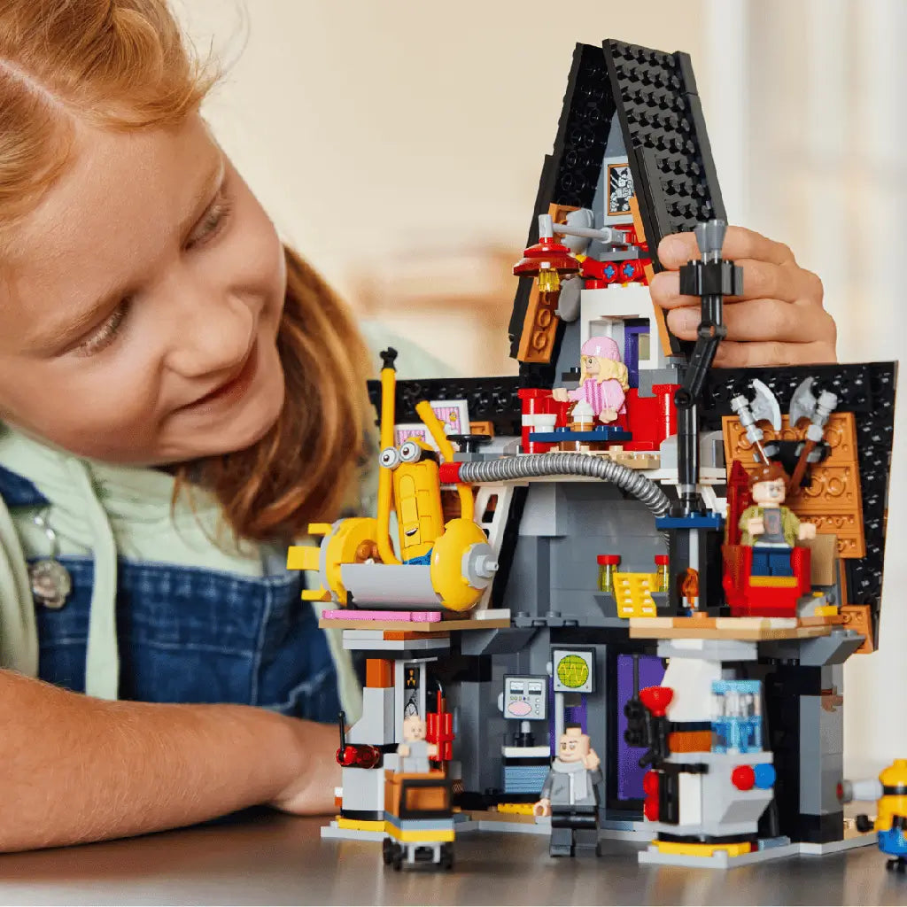 LEGO Despicable Me 4 mansion in gray, black and bright plastic bricks is assembled by a child, with Minions, laboratory equipment and character figures on a table.