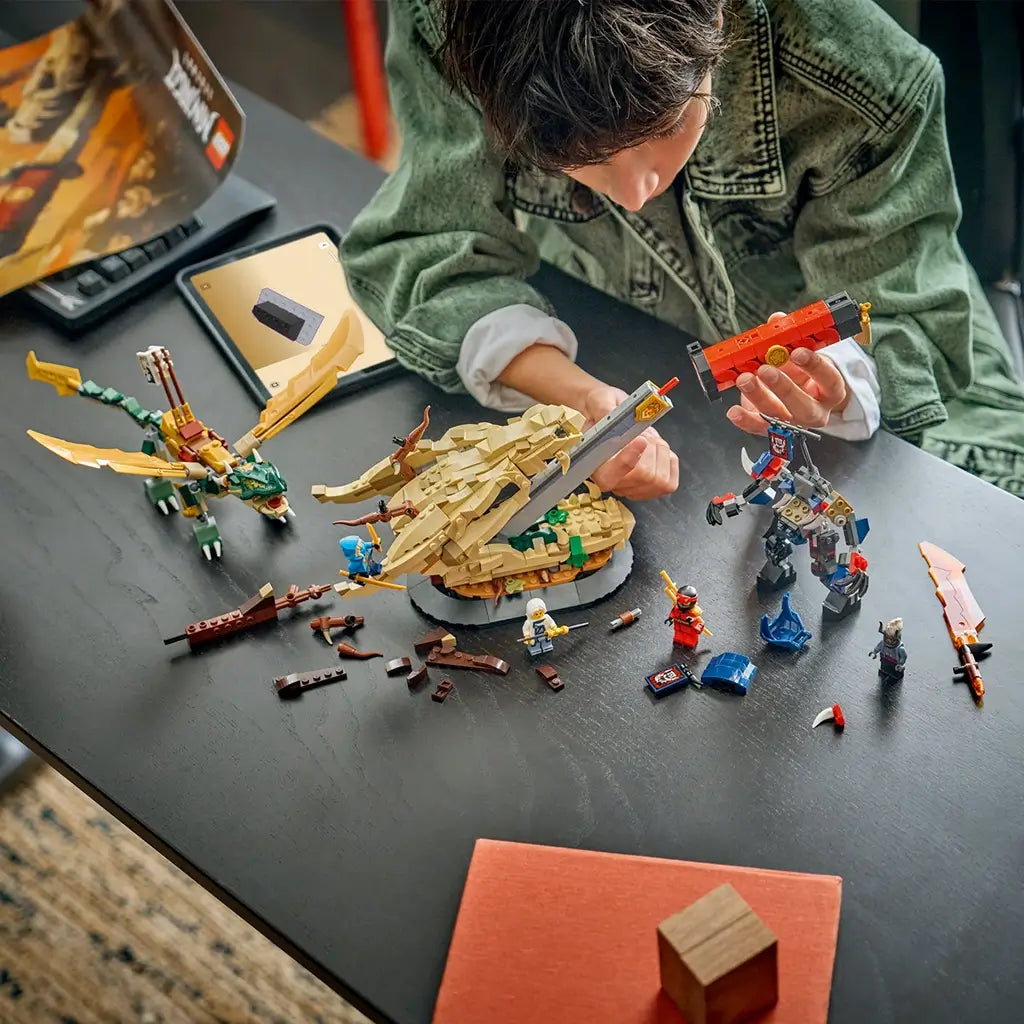 LEGO NINJAGO Battle at the Dragon's Blade in tan, gold, red and blue plastic is assembled on a dark table as a builder holds the sword sheath amid figures and loose pieces.