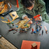 LEGO NINJAGO Battle at the Dragon's Blade in tan, gold, red and blue plastic is assembled on a dark table as a builder holds the sword sheath amid figures and loose pieces.
