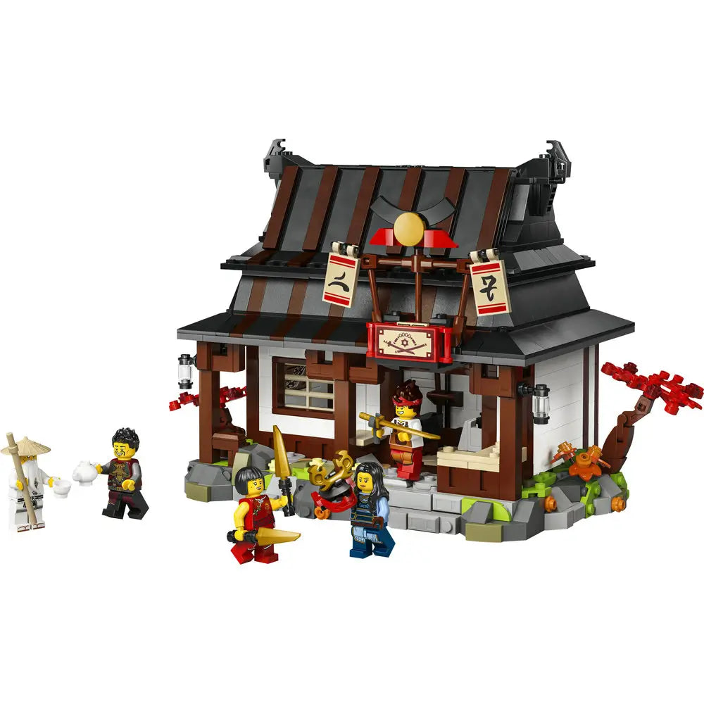 LEGO NINJAGO Legacy Four Weapons Blacksmith building in dark brown, black, gray, and red plastic with a traditional curved roof, hanging banners, stone base, and multiple minifigures gathered outside in a village-style setting on a white background.