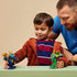 LEGO NINJAGO mech toy in blue and green plastic, small robot figures with movable limbs and weapons, action play scene with a child and adult in a simple indoor setting.
