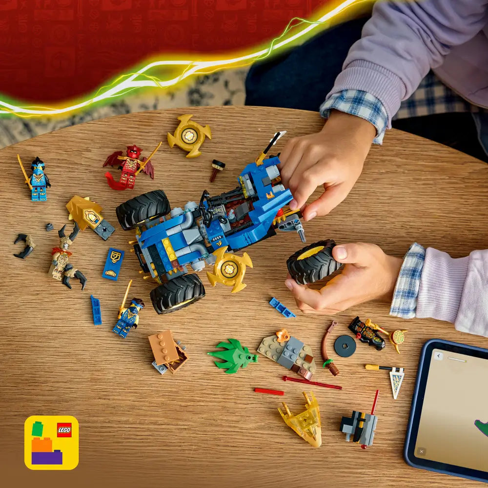 LEGO NINJAGO building toy scene with blue and gold plastic car parts spread on a wooden table, chunky tire pieces, minifigures, and accessories shown mid-build to demonstrate hands-on creative construction play.