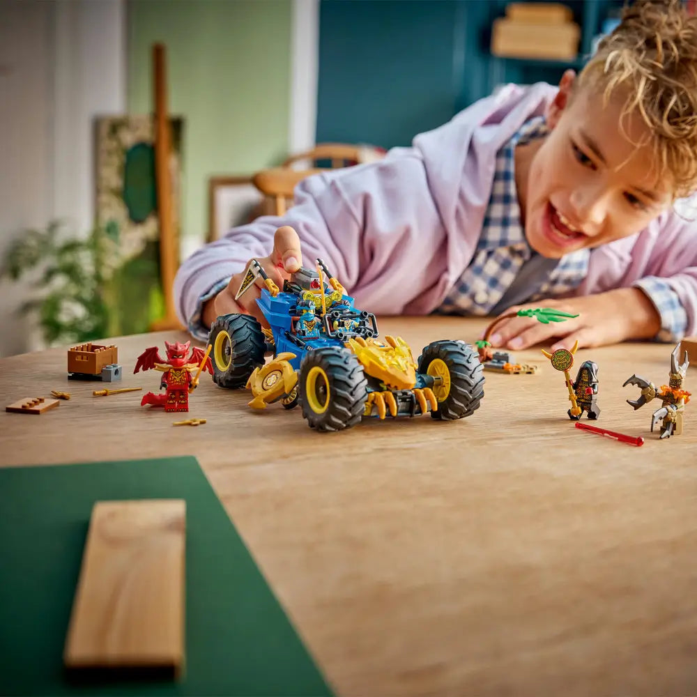 LEGO NINJAGO toy car built from blue and gold plastic with large black tires, shown in use by a child leaning forward with excitement, emphasizing interactive building, storytelling, and creative ninja play.