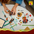 LEGO NINJAGO vehicle set in red, black and gold plastic is spread across a white table as a child builds the buggy and motorcycle beside a tablet with instructions.