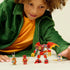 LEGO NINJAGO dragon mech play scene shows a child wearing a green jacket smiling while arranging red and gold plastic mech and ninja minifigures, highlighting imaginative building and hands on play.