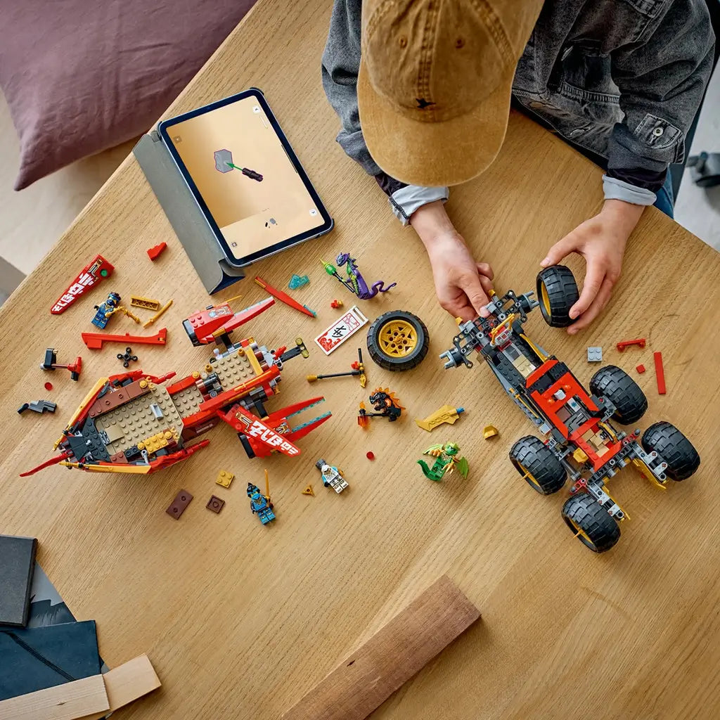 LEGO NINJAGO Land Bounty in red, black and gold plastic is assembled by a builder at a wood table, with the ship, wheeled chassis, minifigures and loose parts nearby.