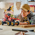 LEGO NINJAGO Land Bounty in red, black and gold plastic sits on six large wheels as a smiling builder plays with the vehicle and minifigures at a light wood table.