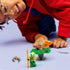 LEGO NINJAGO play scene shows a smiling child in a red hoodie leaning close while spinning a green plastic battle top with minifigures, emphasizing interactive play and imaginative storytelling.