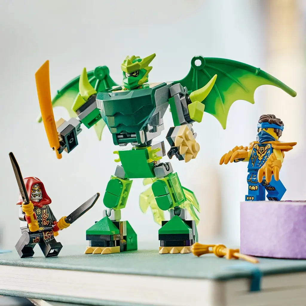 LEGO NINJAGO dragon mech toy in green, gray and gold bricks stands with broad wings and sword, flanked by Lloyd and a hooded villain on books in a bright room.