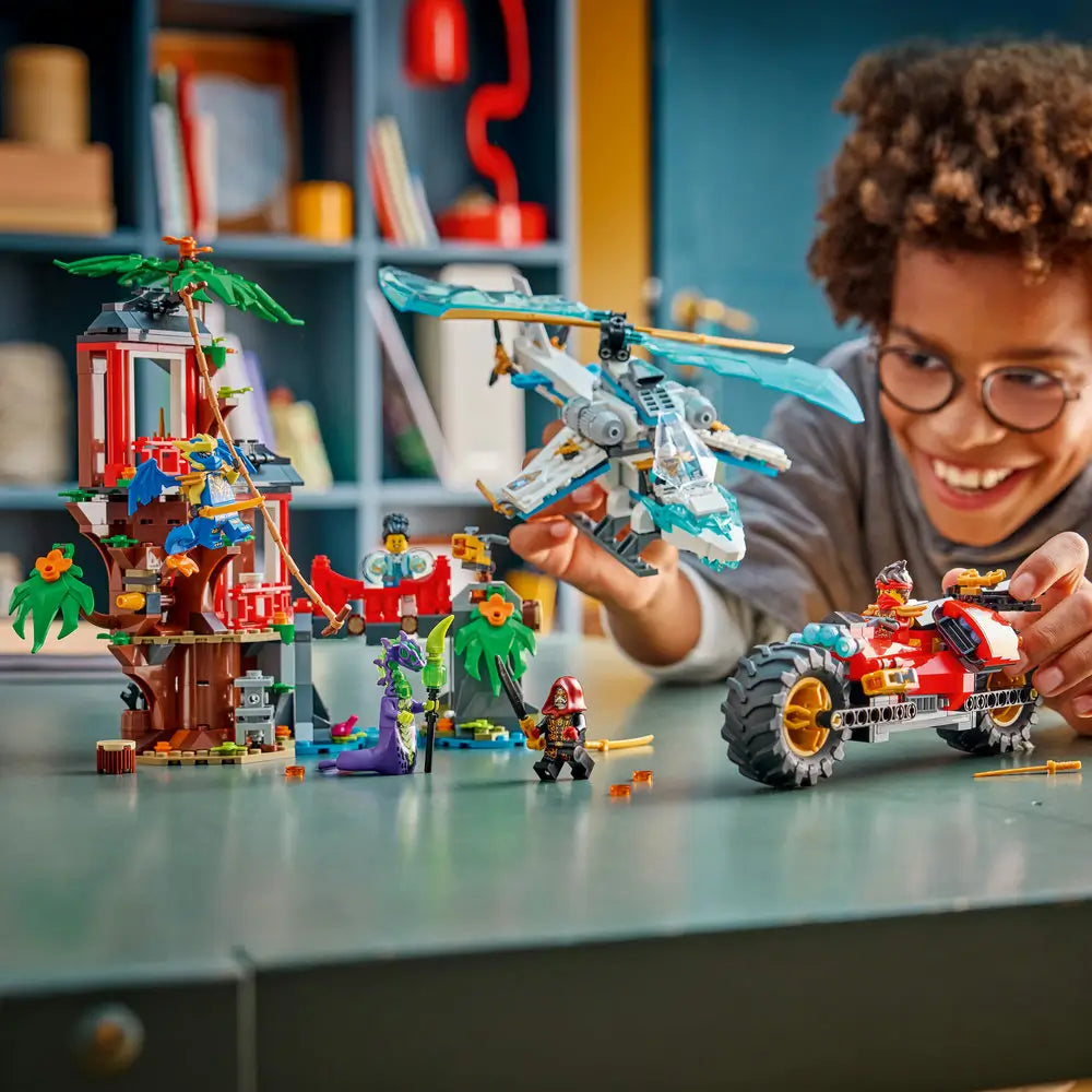 LEGO NINJAGO Dragons Rising set being played with by a child at a table, featuring the tree house, blue dragon aircraft, red ninja vehicle, and minifigures to emphasize hands-on building and imaginative storytelling.