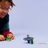 LEGO NINJAGO play scene shows a smiling child wearing glasses leaning in while launching a purple plastic spinner with minifigures, highlighting hands on play, motion action, and imaginative storytelling.