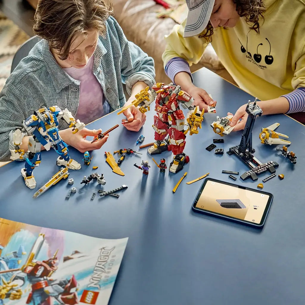 LEGO NINJAGO Twin Titan Mechs in red, blue, white and gold plastic are being assembled by two builders at a table with minifigures, loose parts and digital instructions.