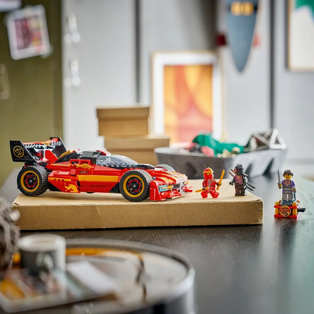 LEGO NINJAGO X-1 Ninja Charger in red, black and gold plastic is displayed on a cardboard box beside three minifigures, with storage bins softly blurred in the background.