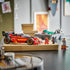 LEGO NINJAGO X-1 Ninja Charger in red, black and gold plastic is displayed on a cardboard box beside three minifigures, with storage bins softly blurred in the background.