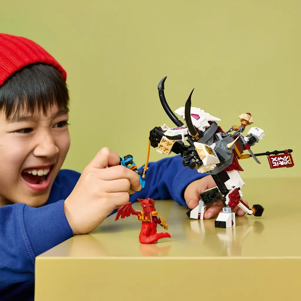 LEGO NINJAGO dragon toy in white, black and red bricks faces a blue minifigure held by a smiling child, with a red winged minifigure on a tan tabletop.