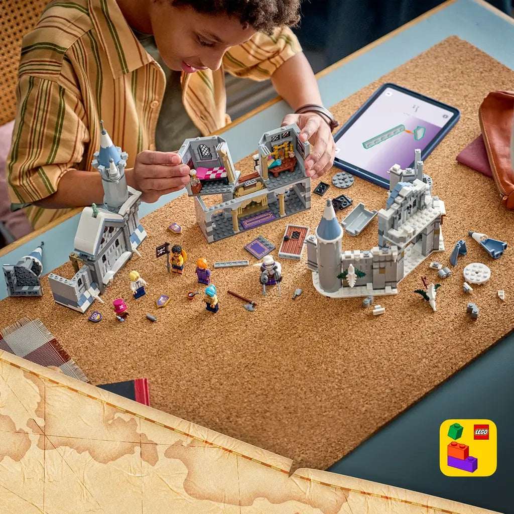 LEGO One Piece Battle at Drum Castle build shows gray plastic castle sections, blue-gray towers, loose bricks, six minifigures, and a digital guide spread across a cork table.