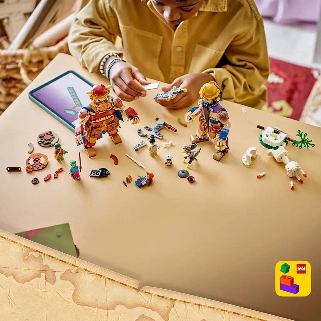 LEGO One Piece Dorry vs. Brogy build shows brown and tan brick-built giants, loose plastic pieces, character figures, white scenery, and a digital guide on a tabletop.