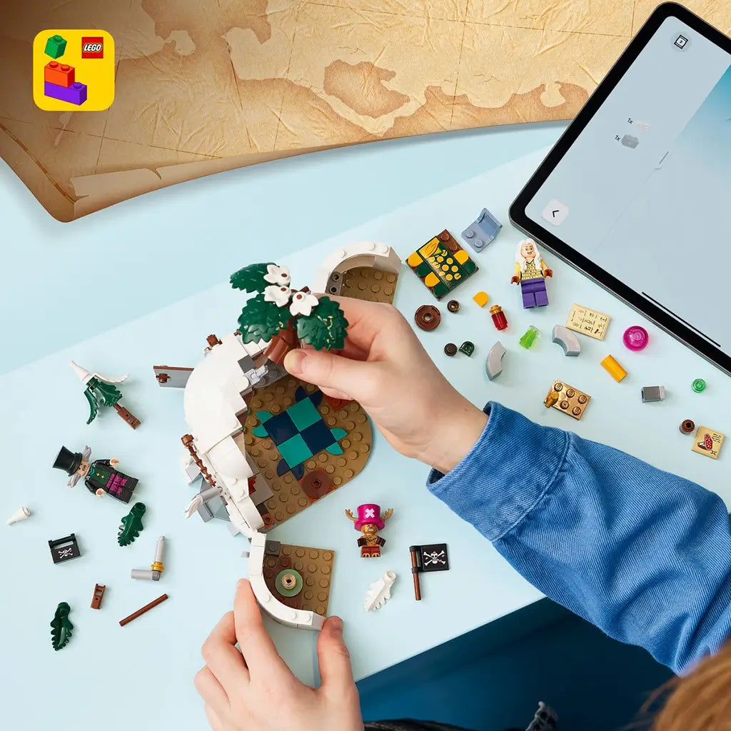 LEGO One Piece building set in white, brown and green plastic is assembled by a child at a blue table, with cave walls, flowering tree, loose pieces and tablet.