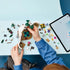 LEGO One Piece building set in white, brown and green plastic is assembled at a blue table, with a flowering tree, cave sections, minifigures and digital instructions.