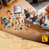 LEGO One Piece Garp's Marine Battleship build in gray, brown, and black bricks sits partly assembled on a wooden table with loose pieces, minifigures, and a digital guide.