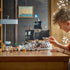 LEGO One Piece Garp's Marine Battleship in gray and brown plastic bricks has tall black sails and minifigures, while a young builder plays with the ship at a wooden table.