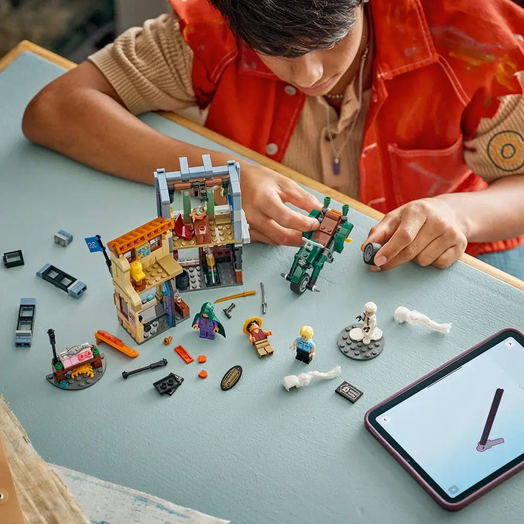 LEGO One Piece playset in gray, tan, orange and green plastic shows a smiling builder moving the motorcycle beside the Recruitment Center, stall and minifigures.