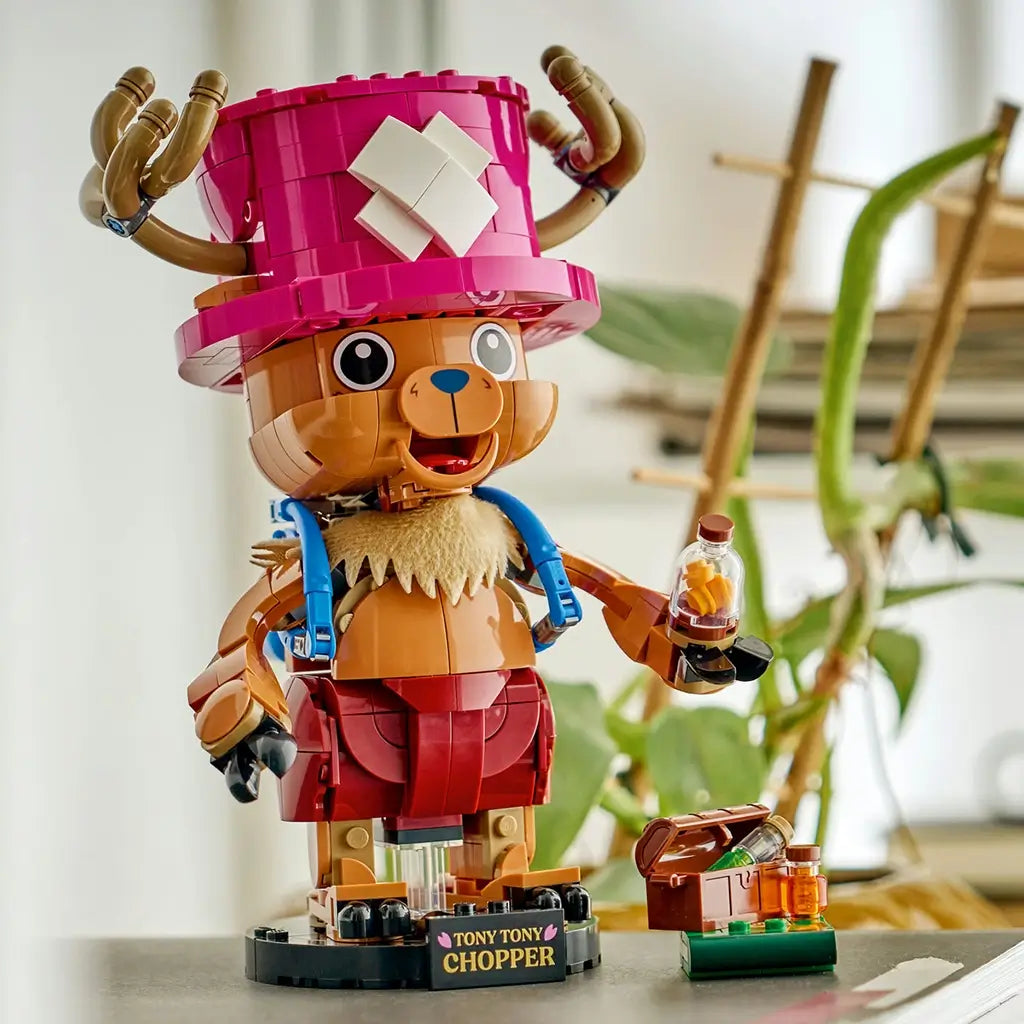LEGO One Piece Tony Tony Chopper display features a brown brick-built figure with pink hat and blue backpack holding a medicine bottle beside a small treasure chest.
