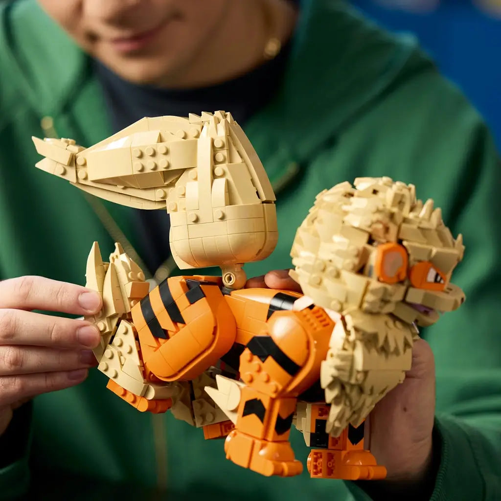 LEGO Pokémon Arcanine build in orange, tan, and black plastic bricks is held by an adult, highlighting the articulated curled tail, striped body, layered mane, and sturdy legs.