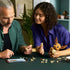 LEGO Pokémon Eevee building set shows brown and cream plastic pieces, curved character components and articulated sections, assembled by builders at a table with instructions and parts nearby.