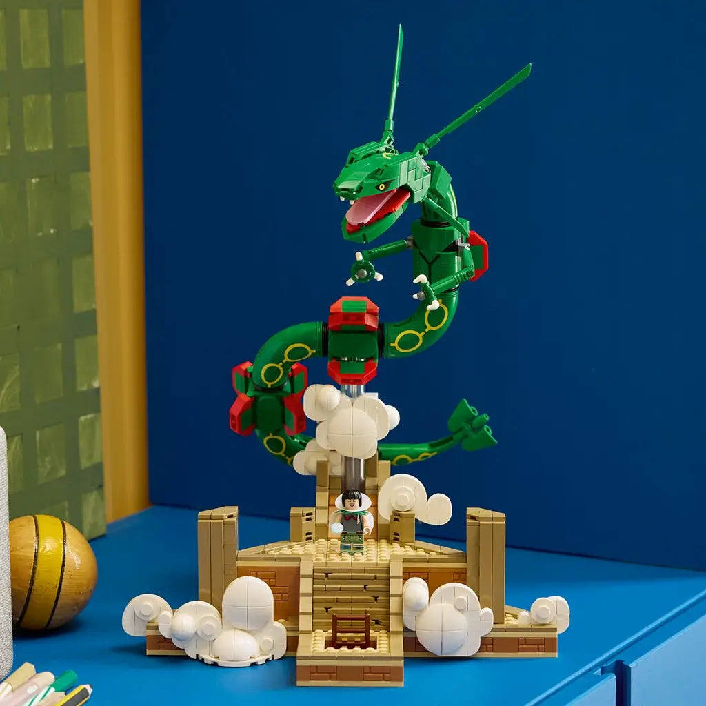 LEGO Pokémon Rayquaza display features a green brick-built dragon with red accents above a tan shrine and white clouds, staged on a blue surface against a dark blue wall.
