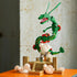 LEGO Pokémon Rayquaza display in green, red, tan, and white bricks features the articulated dragon above a cloud-covered shrine and trainer minifigure on an orange surface.
