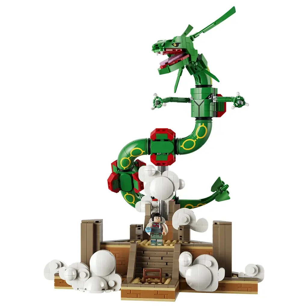 LEGO Pokémon Rayquaza model in green, red, and yellow plastic bricks curves above a tan shrine and white clouds, with a trainer minifigure centered on the steps.
