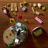 LEGO Shrek building set is shown partly assembled from above on a wooden table, with gray Donkey, orange Puss in Boots, colorful bricks, flowers and a Beware Ogre sign.