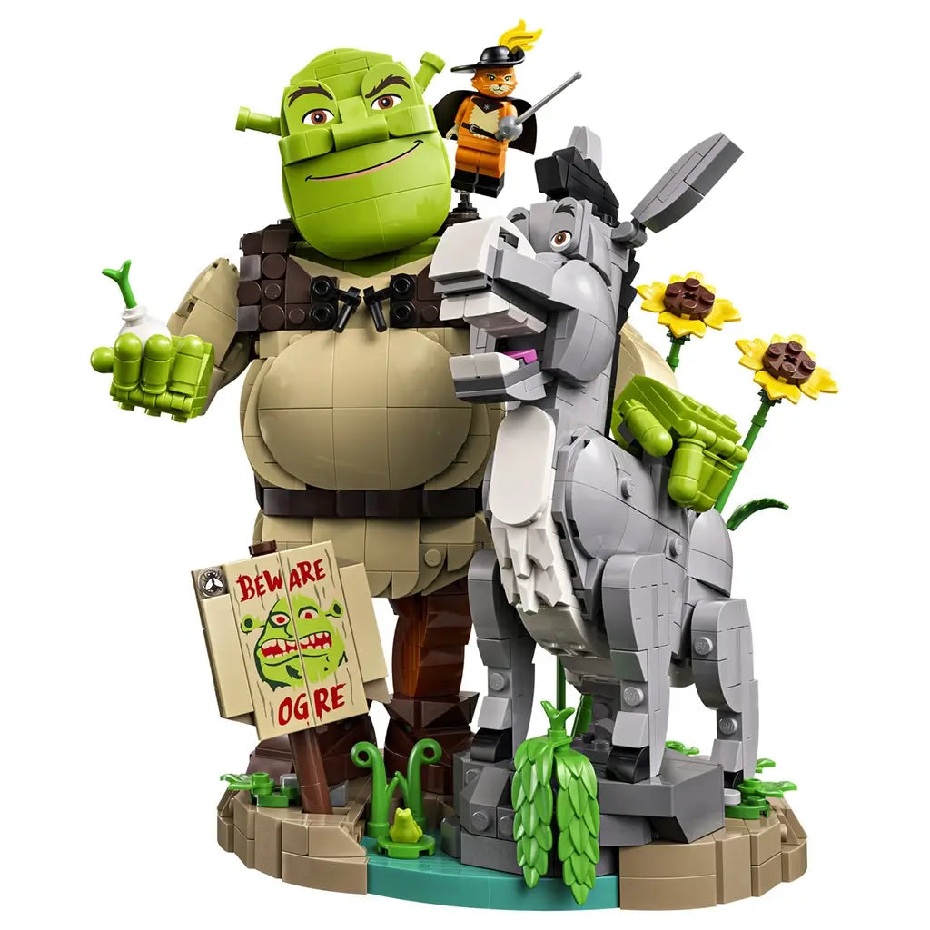 LEGO Shrek display model features green Shrek holding an onion beside gray Donkey and orange Puss in Boots, with sunflowers and a Beware Ogre sign on a swamp base.