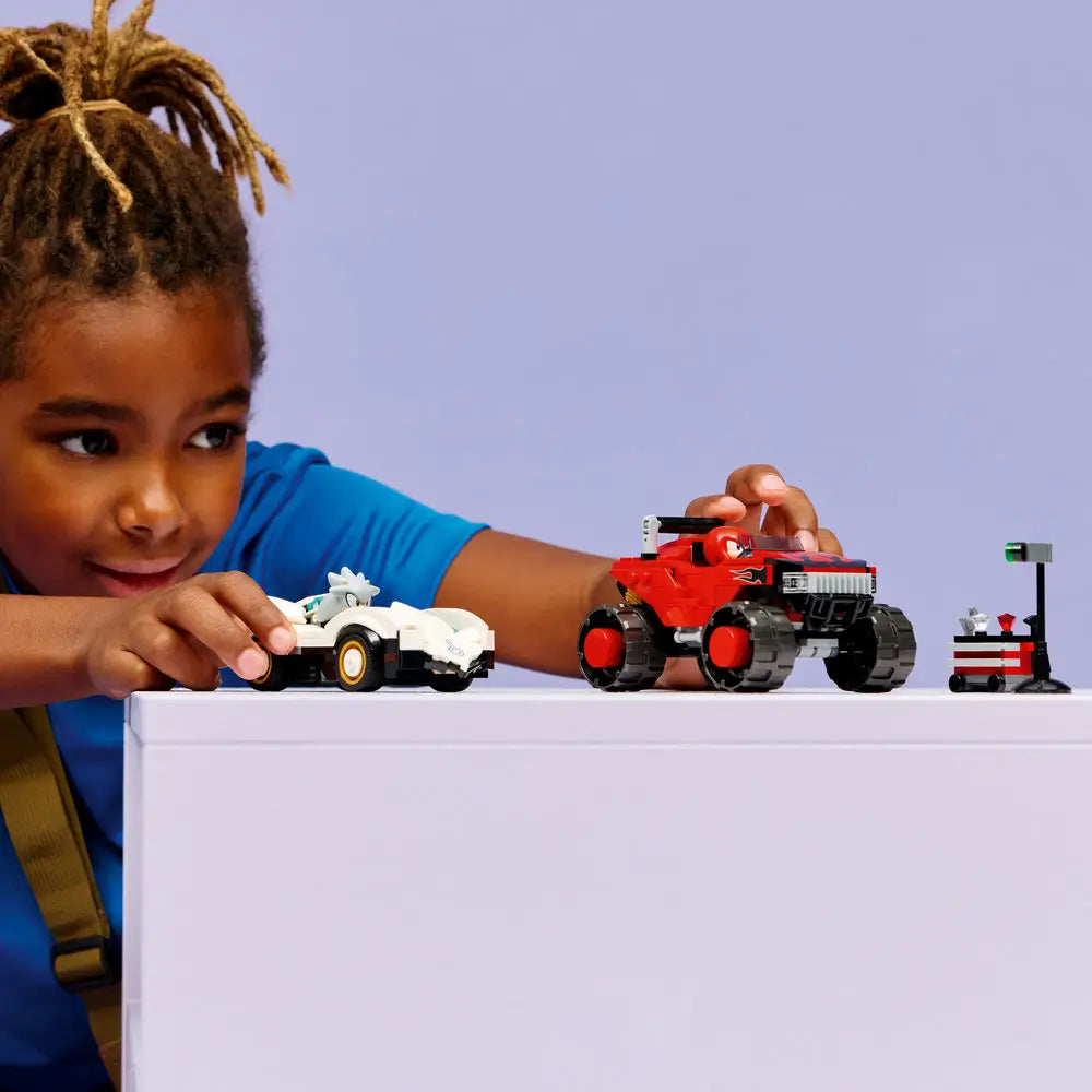 Child assembling LEGO Sonic the Hedgehog Knuckles’ Monster Truck made of red plastic with oversized wheels and a blocky off-road shape, holding pieces at hand scale to show interactive building and creative play.