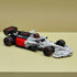 LEGO Audi F1 race car model in gray, black, and red plastic bricks, low aerodynamic shape with detailed tires and rear wing, displayed on a plain surface with soft neutral background.