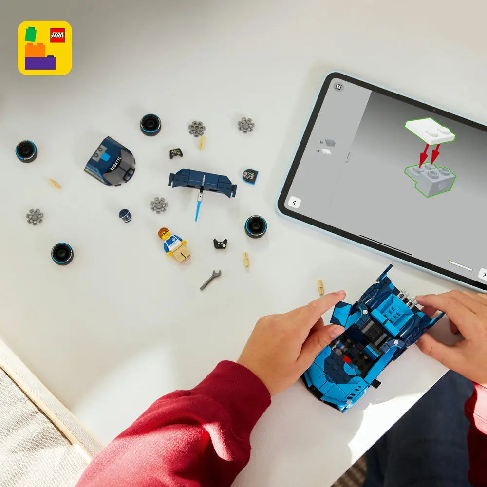 LEGO Bugatti Vision Gran Turismo building pieces in blue and black plastic with round wheels, minifigure parts, and small connectors, arranged flat for assembly, showing the full construction set laid out on a light tabletop surface.