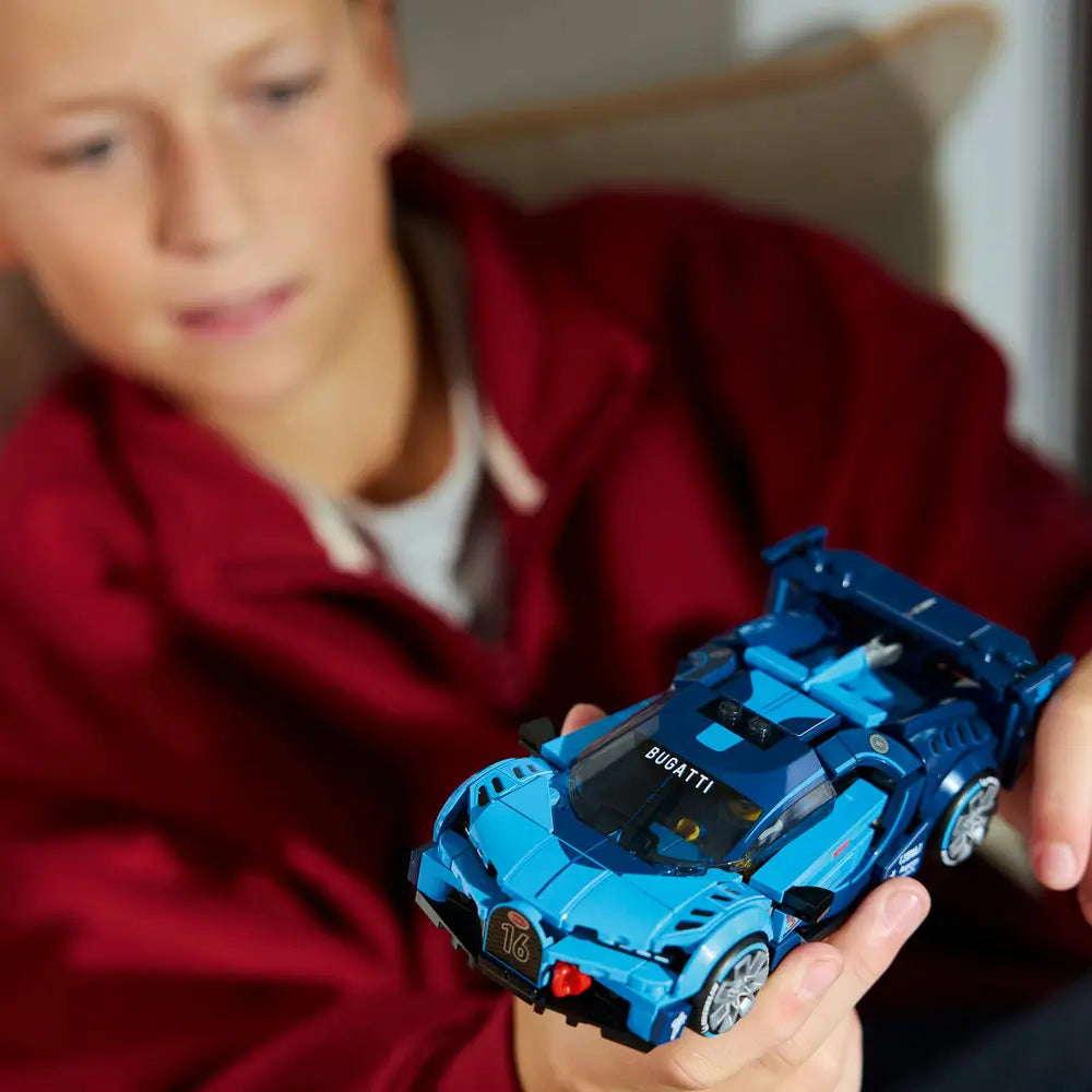 Child holding a LEGO Bugatti Vision Gran Turismo car made of blue plastic with sleek racing shape and rear wing, shown at hand scale to highlight finished details and imaginative play in a softly lit indoor setting.