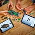 LEGO Speed Champions Aston Martin Aramco F1 model in green and black plastic with detachable race car parts being assembled by multiple hands beside tablets showing digital building instructions.