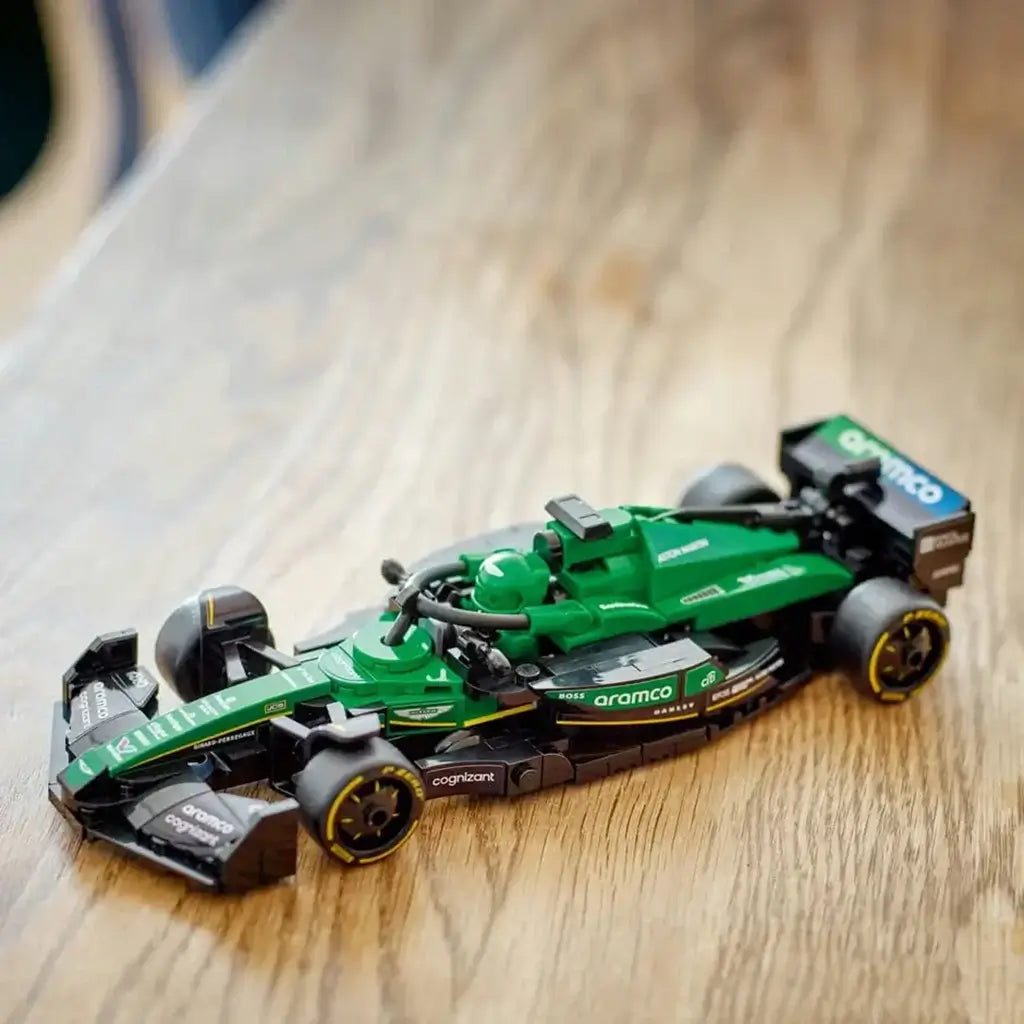 LEGO Speed Champions Aston Martin Aramco F1 model in green and black plastic with detailed open-wheel race car design displayed on a wooden tabletop against a softly blurred indoor background.