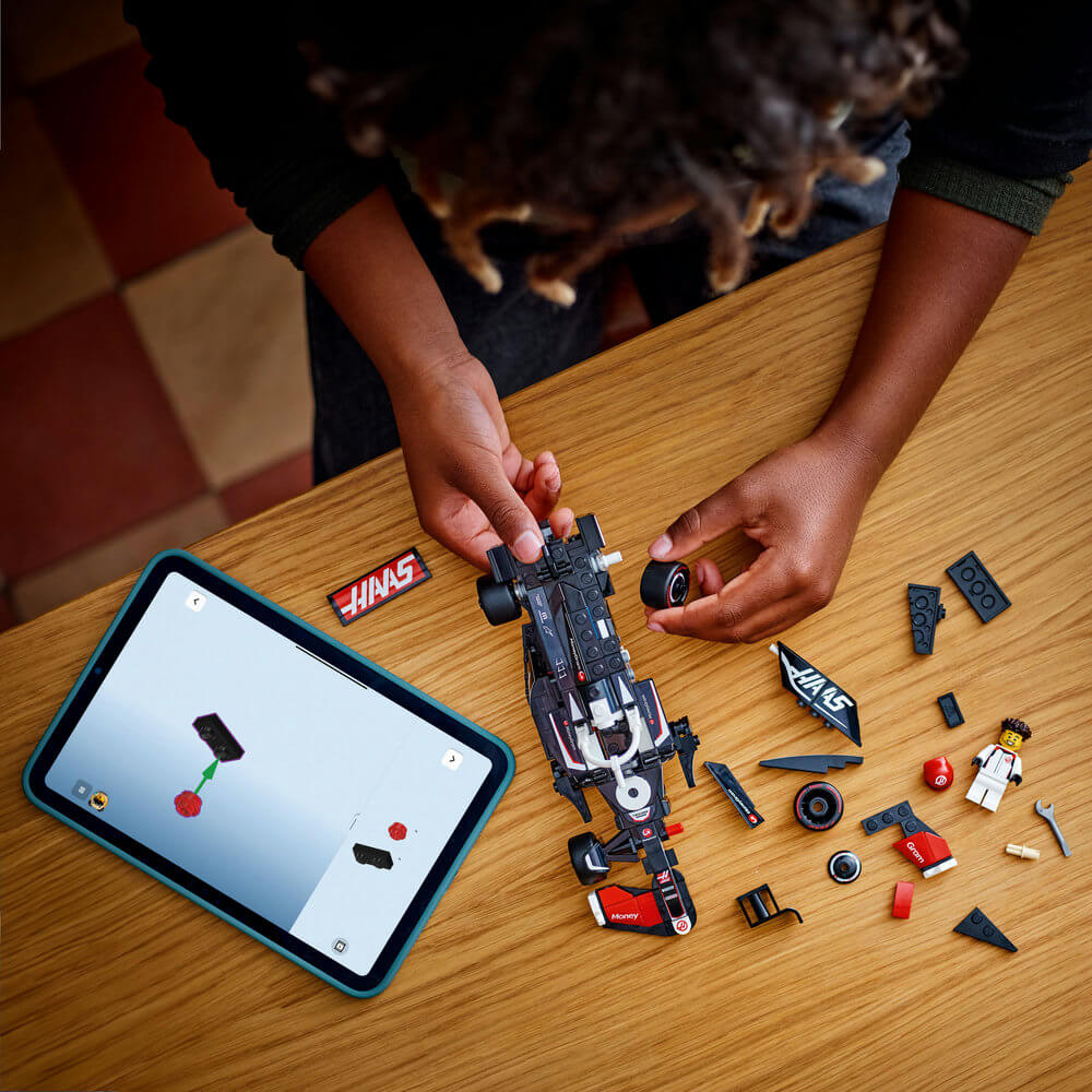 LEGO Speed Champions MoneyGram Haas F1 Team VF-24 black race car is assembled with loose pieces beside digital instructions on a tablet across a wooden tabletop with authentic sponsor graphics.