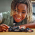 LEGO Speed Champions MoneyGram Haas F1 Team VF-24 black and red race car is pushed by a smiling child across a wooden tabletop during imaginative indoor play with authentic sponsor graphics.