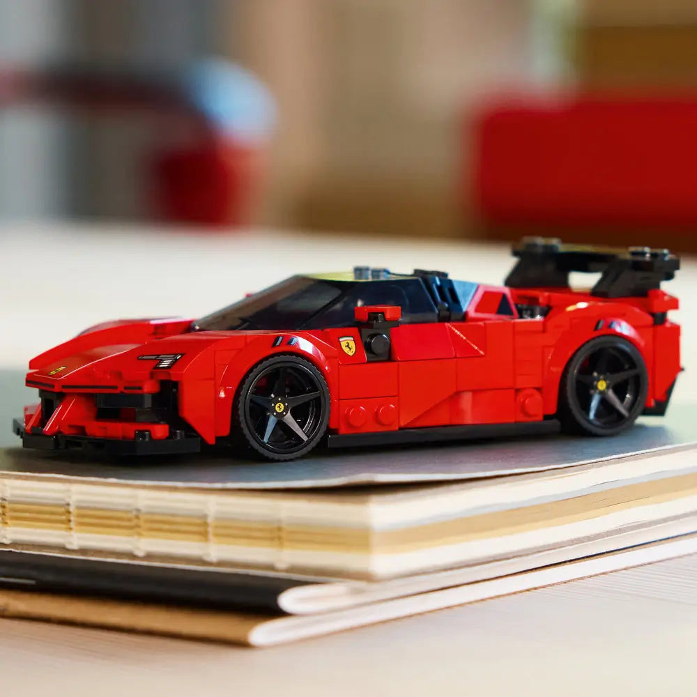 Completed LEGO Ferrari SF90 XX Stradale displayed on stacked notebooks, showing the sleek red body, black aerodynamic features, low stance, and detailed wheels in a styled lifestyle scene