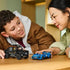 LEGO Speed Champions Jaguar and Land Rover models in blue and black plastic sit on a wooden table as a child and adult play with the brick-built vehicles together indoors.