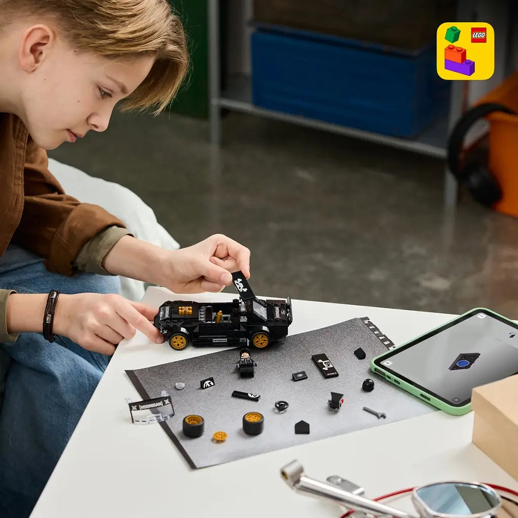LEGO Speed Champions Ford Mustang Hoonicorn in black plastic is assembled by a young builder at a table with gold wheels, loose pieces, minifigure and a tablet nearby.